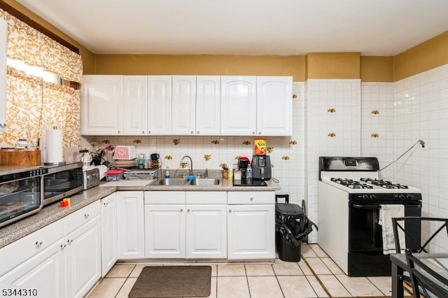 kitchen with a sink, gas stove, tile walls, white cabinets, and light tile patterned flooring