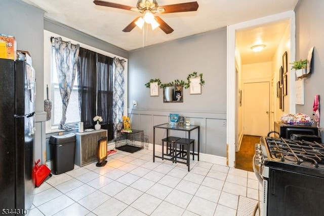 kitchen featuring light tile patterned floors, a ceiling fan, a wainscoted wall, stainless steel range with gas cooktop, and freestanding refrigerator