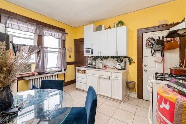 kitchen featuring radiator heating unit, light countertops, light tile patterned floors, white appliances, and white cabinetry