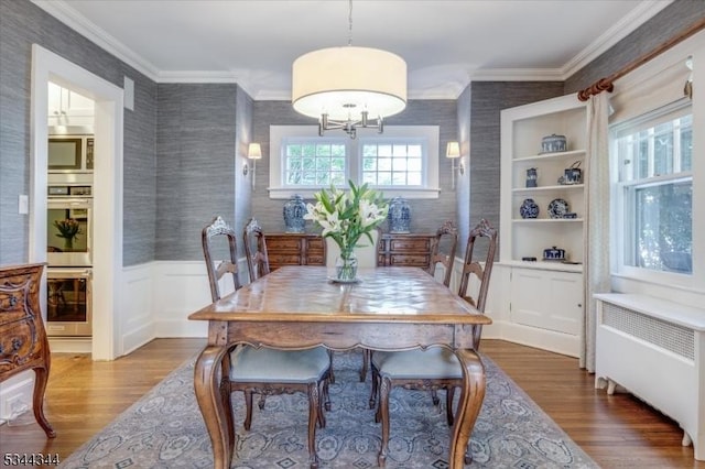 dining area with crown molding, radiator, dark wood-style flooring, wallpapered walls, and a wainscoted wall