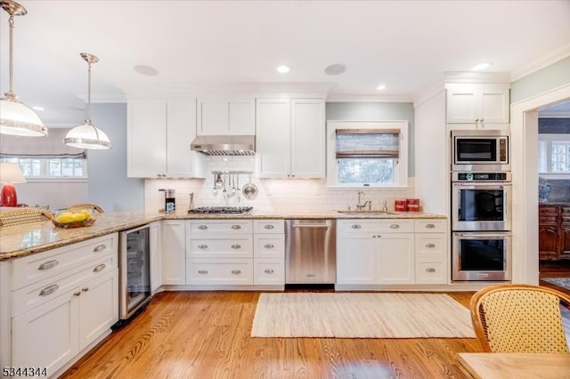 kitchen featuring white cabinets, appliances with stainless steel finishes, a sink, light wood finished floors, and wine cooler