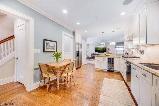 kitchen with a peninsula, beverage cooler, light wood-style floors, white cabinetry, and appliances with stainless steel finishes