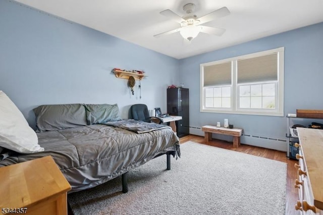 bedroom featuring a ceiling fan, baseboard heating, and wood finished floors