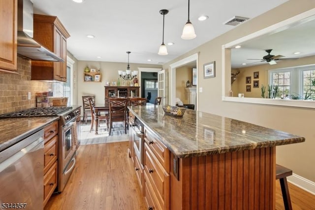 kitchen featuring visible vents, a breakfast bar area, light wood-type flooring, wall chimney exhaust hood, and stainless steel appliances