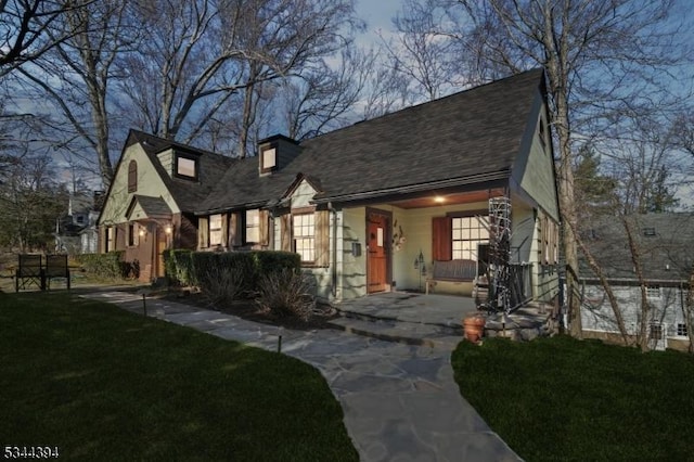 view of front facade featuring a front lawn, covered porch, and roof with shingles