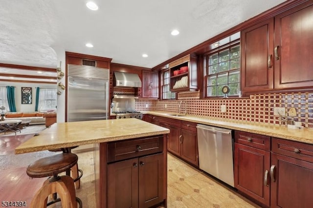 kitchen with wall chimney exhaust hood, a kitchen breakfast bar, tasteful backsplash, recessed lighting, and appliances with stainless steel finishes