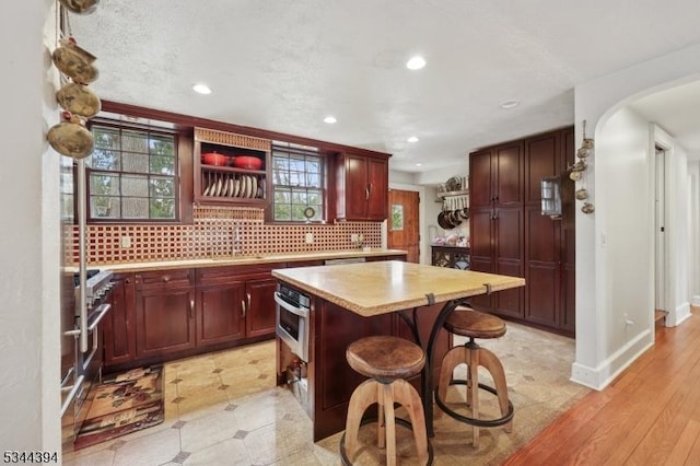 kitchen with recessed lighting, light countertops, open shelves, reddish brown cabinets, and appliances with stainless steel finishes