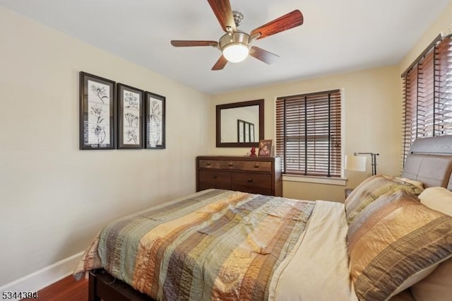 bedroom featuring baseboards, a ceiling fan, wood finished floors, and multiple windows