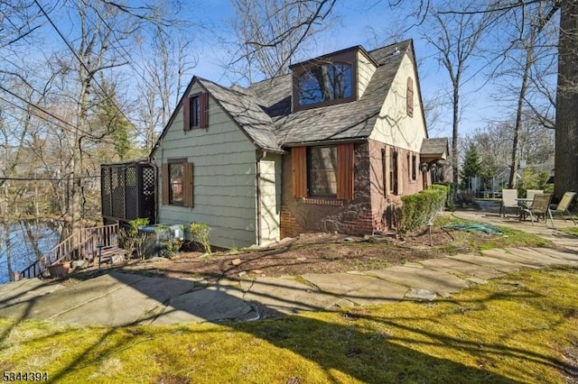 view of side of property featuring a patio area and a shingled roof