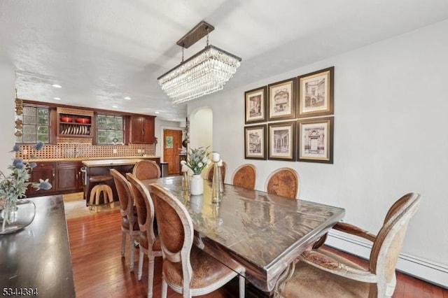 dining room featuring recessed lighting, wood finished floors, arched walkways, a baseboard radiator, and a notable chandelier