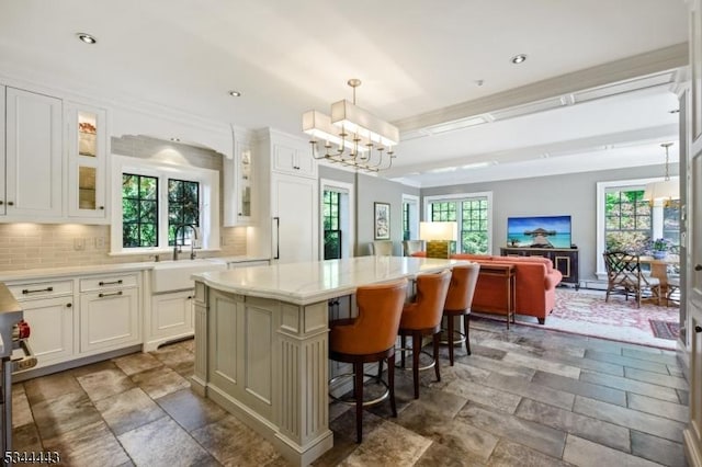 kitchen with an inviting chandelier, decorative backsplash, a kitchen island, glass insert cabinets, and a sink