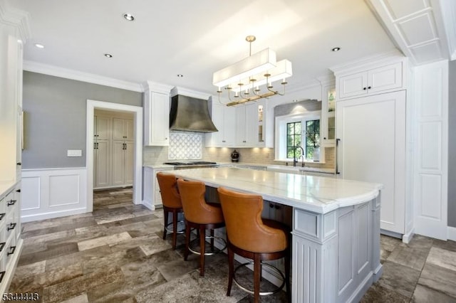 kitchen featuring white cabinetry, a kitchen island, wall chimney range hood, and glass insert cabinets