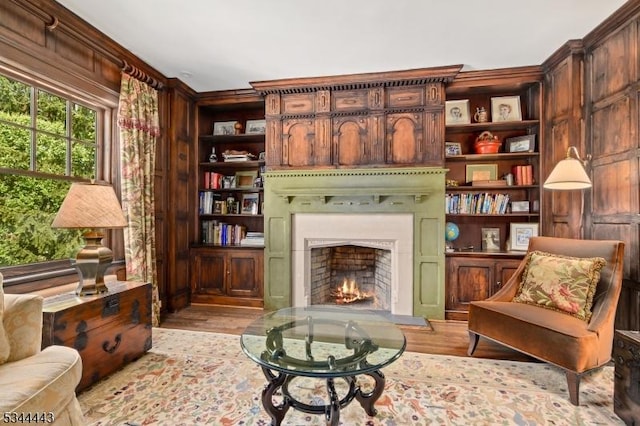 sitting room featuring light wood-style floors, ornamental molding, built in features, and a lit fireplace