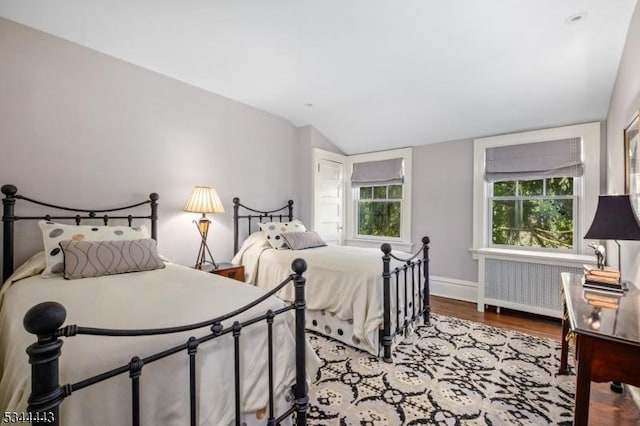 bedroom featuring baseboards, vaulted ceiling, radiator heating unit, and wood finished floors