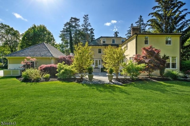 rear view of house with french doors, stucco siding, a yard, and a chimney