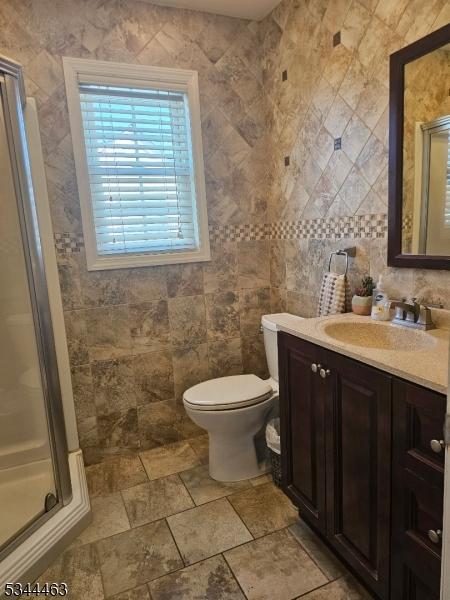 bathroom featuring vanity, tile walls, toilet, and a shower stall