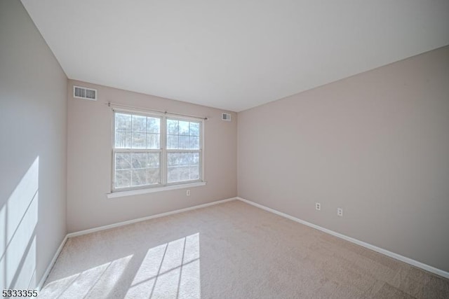 empty room featuring light carpet, visible vents, and baseboards