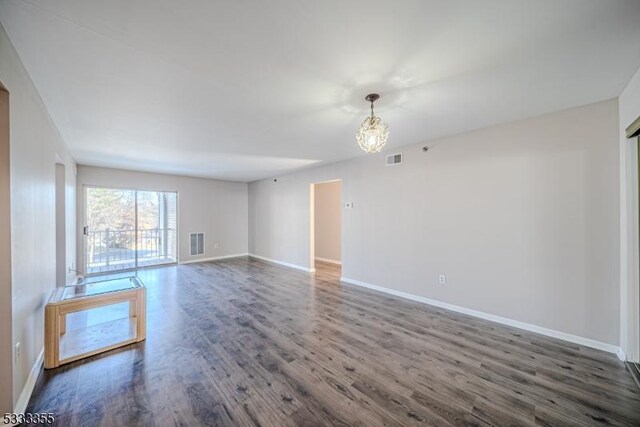unfurnished room with a notable chandelier, visible vents, baseboards, and wood finished floors