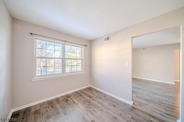 spare room with visible vents, baseboards, and wood finished floors