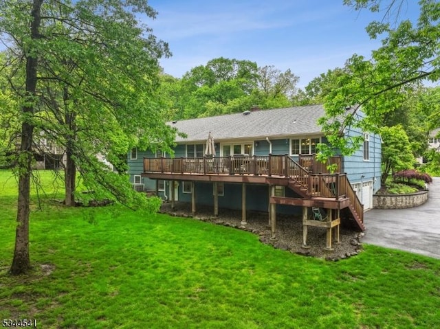 back of property featuring driveway, a wooden deck, a yard, stairway, and an attached garage