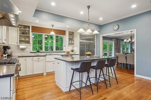kitchen featuring high quality appliances, a sink, wall chimney range hood, backsplash, and dark countertops