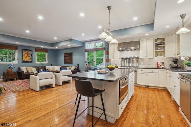 kitchen featuring stainless steel appliances, wall chimney exhaust hood, dark countertops, light wood-style floors, and a center island
