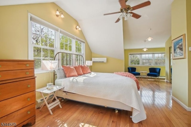 bedroom with light wood-style floors, baseboards, a wall unit AC, and vaulted ceiling
