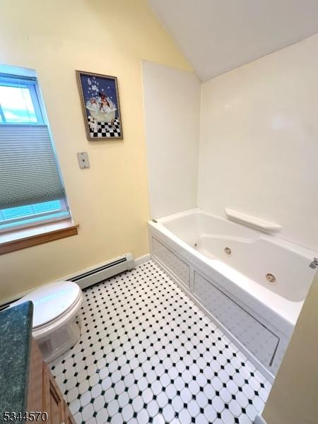 bathroom featuring toilet, vaulted ceiling, a jetted tub, and a baseboard radiator