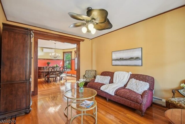 living room with a baseboard radiator, light wood-style flooring, ceiling fan with notable chandelier, and ornamental molding
