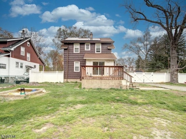 rear view of house featuring a gate, fence, solar panels, a lawn, and a deck