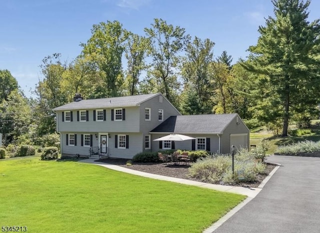 view of front facade featuring a garage, driveway, a front lawn, and a chimney