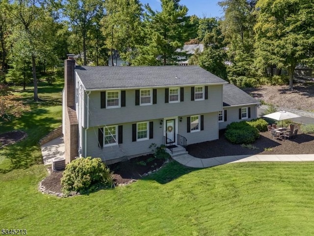 colonial inspired home featuring a chimney, a front lawn, and central AC unit