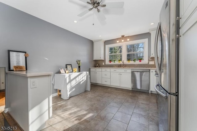 kitchen featuring appliances with stainless steel finishes, a sink, tasteful backsplash, white cabinets, and a ceiling fan
