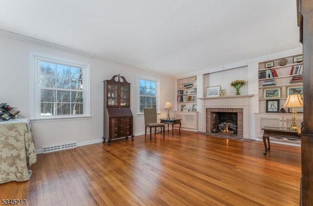 living room with hardwood / wood-style floors, a brick fireplace, crown molding, baseboards, and built in features