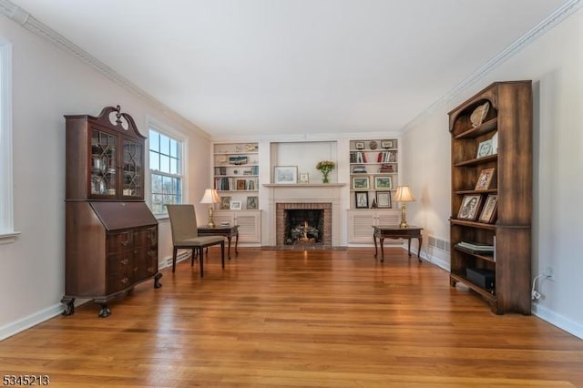 sitting room with light wood-style floors, built in shelves, a fireplace, baseboards, and crown molding