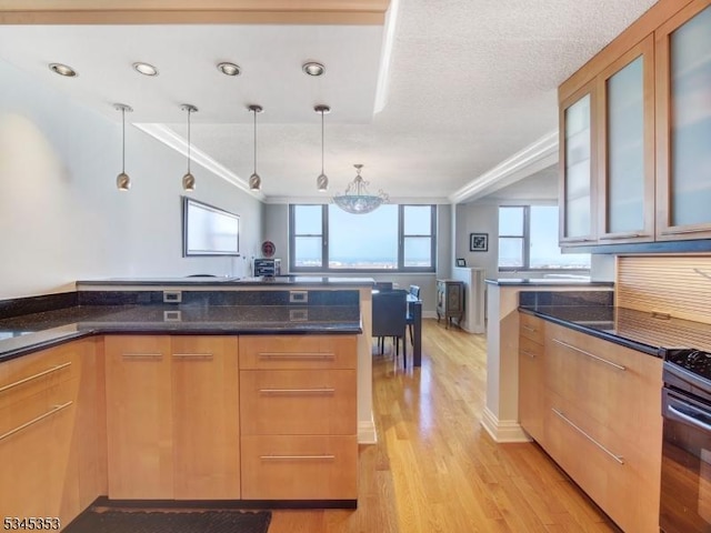 kitchen with dark stone counters, glass insert cabinets, black range with gas stovetop, pendant lighting, and light wood-type flooring