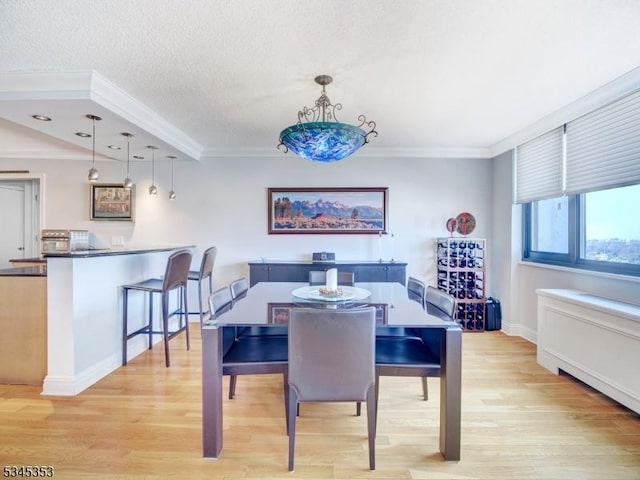 dining space featuring a textured ceiling, light wood-style floors, baseboards, and ornamental molding