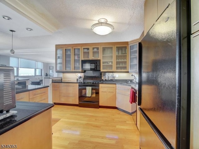 kitchen with a sink, dark countertops, black appliances, and light wood finished floors