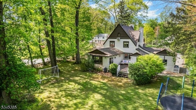 110 Kenilworth Rd, Mountain Lakes Boro, NJ 07046 - back of property with a chimney, a trampoline, a wooden deck, stucco siding, and a lawn