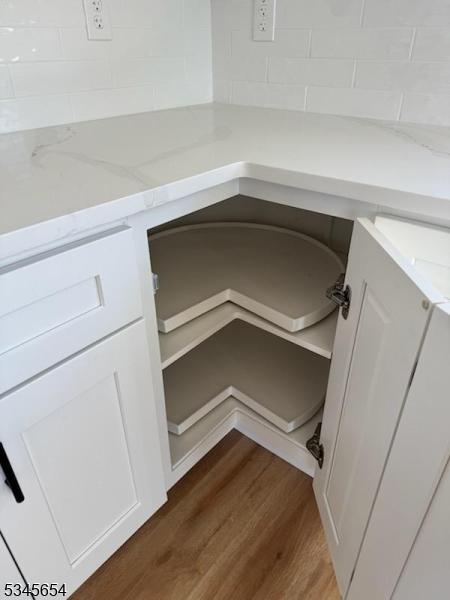 interior details with backsplash, white cabinets, light stone counters, and wood finished floors