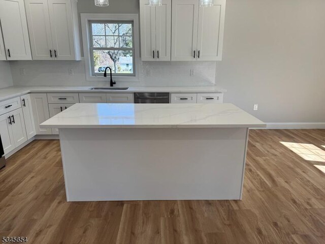 kitchen with decorative backsplash, a kitchen island, a sink, light wood finished floors, and dishwashing machine