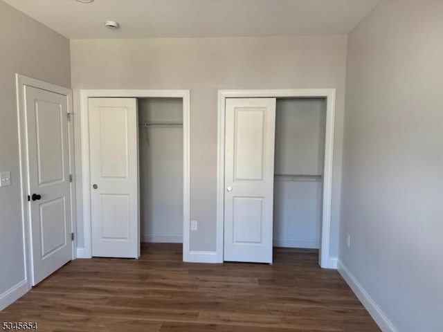 unfurnished bedroom featuring baseboards, multiple closets, and dark wood-type flooring