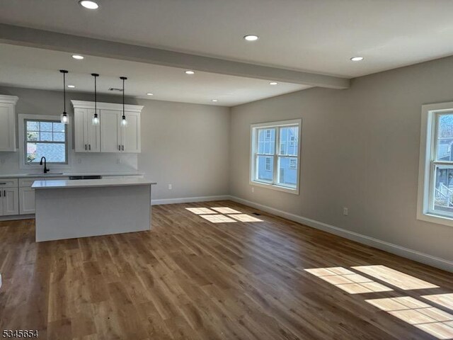 kitchen with a sink, beam ceiling, baseboards, and dark wood finished floors