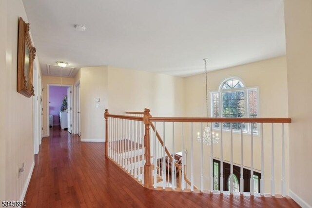 hallway featuring baseboards, attic access, an upstairs landing, and hardwood / wood-style flooring