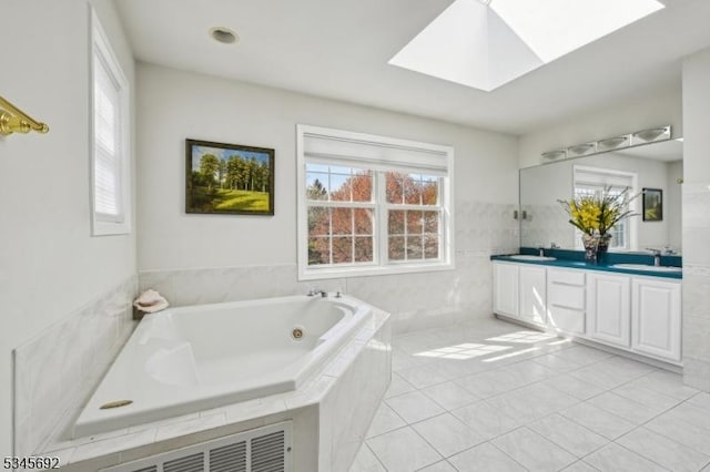 bathroom with a tub with jets, a skylight, a sink, and double vanity