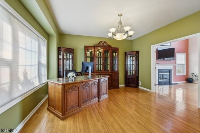 office with a glass covered fireplace, an inviting chandelier, light wood-style flooring, and baseboards