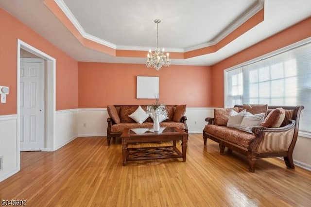 living area with a chandelier, light wood-style floors, a tray ceiling, crown molding, and a wainscoted wall