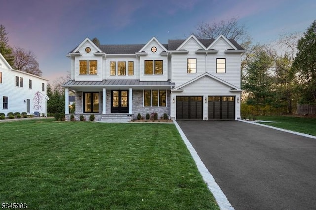 modern farmhouse with a porch, a standing seam roof, driveway, a garage, and a yard