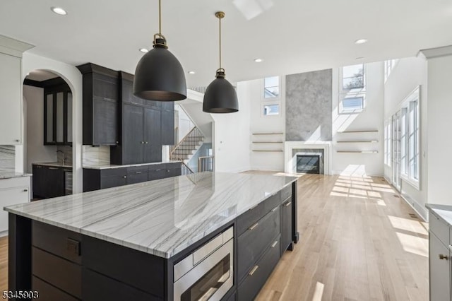 kitchen with light wood-type flooring, recessed lighting, a center island, stainless steel microwave, and hanging light fixtures