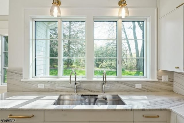 kitchen with white cabinets, light stone counters, pendant lighting, and a sink
